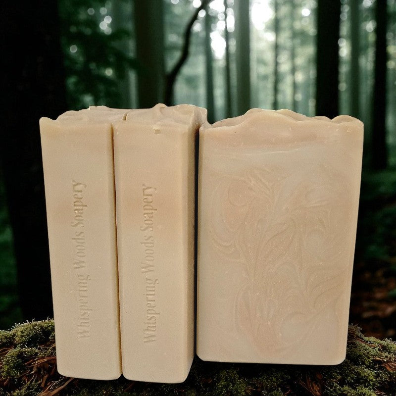 Three bars of creamy tan soap with coppery swirls placed on a forest floor. The bars are stamped Whispering Woods Soapery.