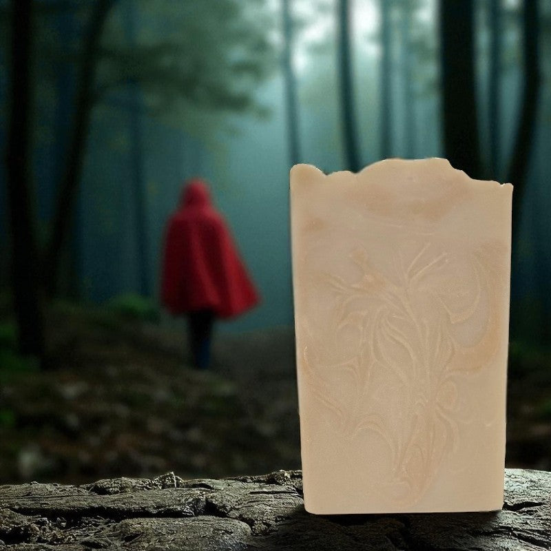 A red-hooded figure walks in the woods. There is a creamy tan soap with coppery swirls in the foreground.