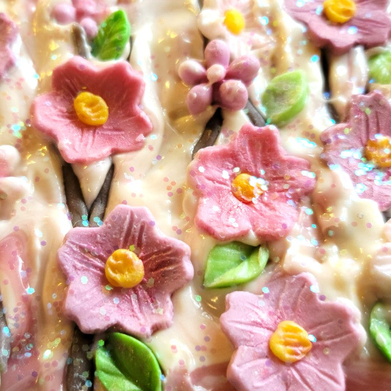 Pink flowers, green petals and glitter sit atop a freshly-poured white soap top