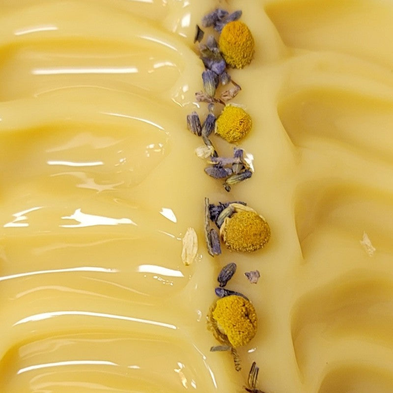 Close-up of wet soap that is colored yellow, with chamomile and lavender topping