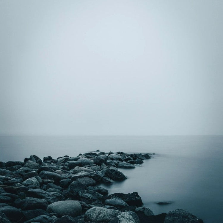 A shelf of large black stones jutting out into the sea on a foggy day