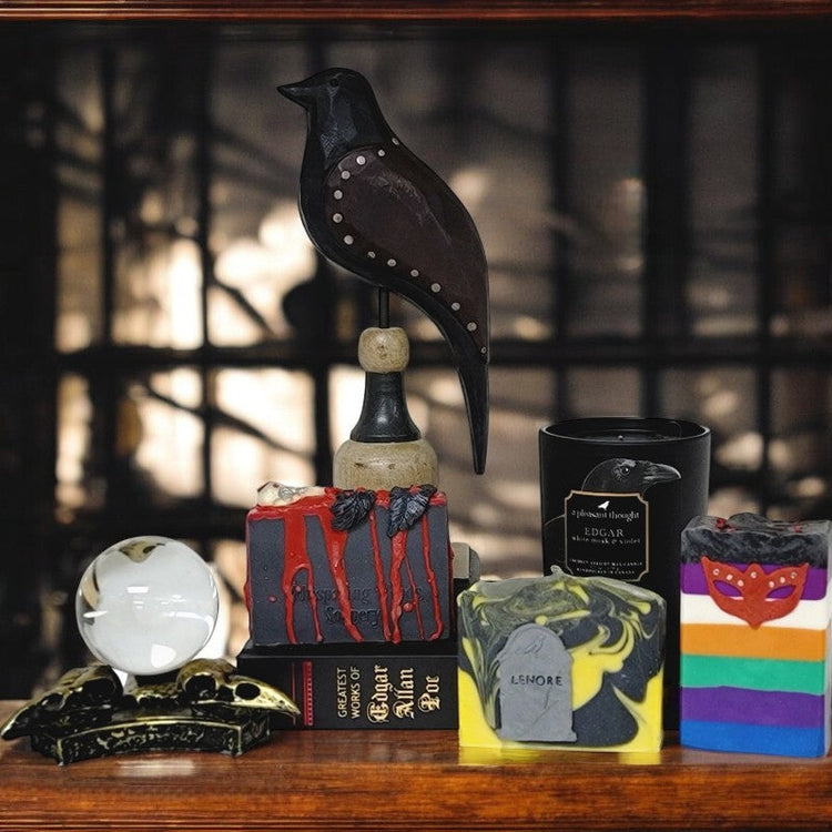 Three soaps by Whispering Woods Soapery sit on a desk with a raven wooden figurine, a candle, and a crystal ball held by raven skulls