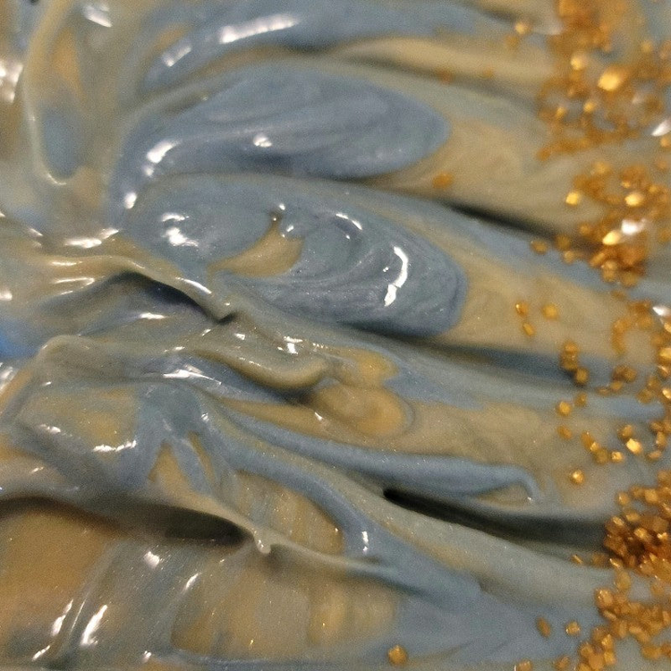 Close-up of freshly poured soap that has blue and gold swirls with gold sugar beads down the right side