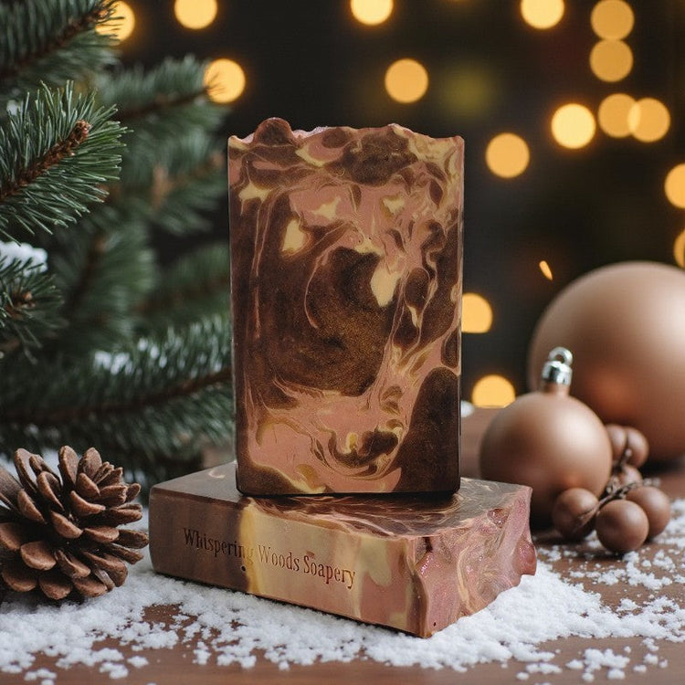 Two cream and brown soap bars in a holiday setting, with pinecones, ornaments, soft lights and a pine tree