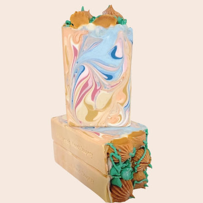 Three soap bars with colored swirls of gold, white, orange, blue and pink, with piped orange pumpkins and green leaves/vines on top