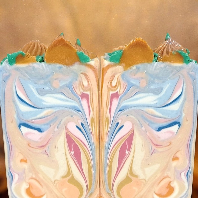 Two soap bars with colored swirls of gold, white, orange, blue and pink, with piped orange pumpkins and green leaves/vines on top