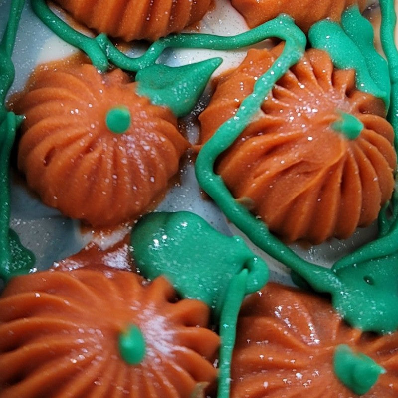 Extreme close-up of freshly piped orange pumpkins with green leaves and vines and silver glitter