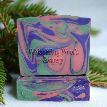 Two bars of soap with pink, purple and green swirls with a balsam branch in the background