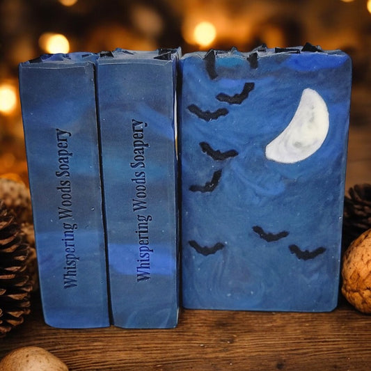 Three blue bars of soap with seven small bats and a crescent moon embed on a wood table with pinecones and nuts