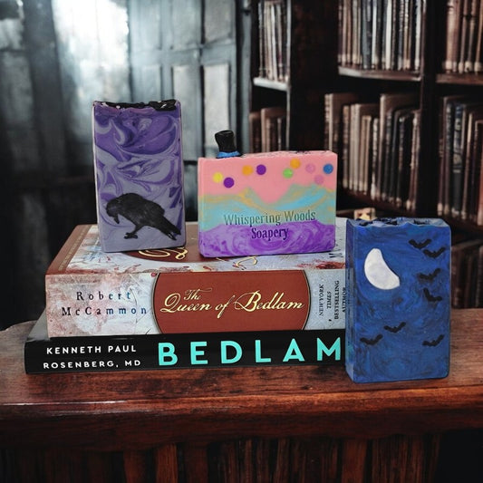 Books about Bedlam in a dark old library with three different soap bars made by Whispering Woods Soapery in the picture