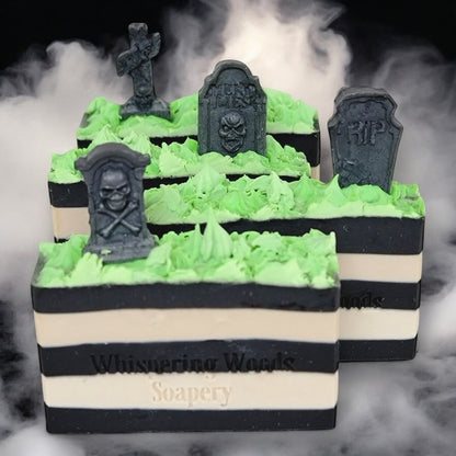 Four bars of soap with black and white stripes, topped with neon green grass and tombstones