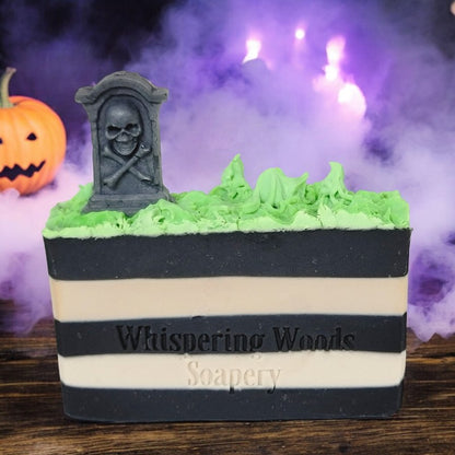 A bar of soap with black and white stripes, topped with neon green grass and a tombstone. There is a jack-o-lantern and purple fog in the background.