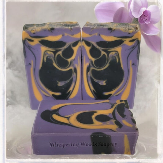 Purple and black soap bar with gold swirls, branded 'Whispering Woods Soapery', on a white background.