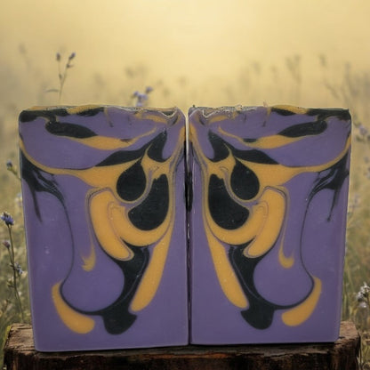 Two soap bars with purple, gold, and black design on a stump with a natural background