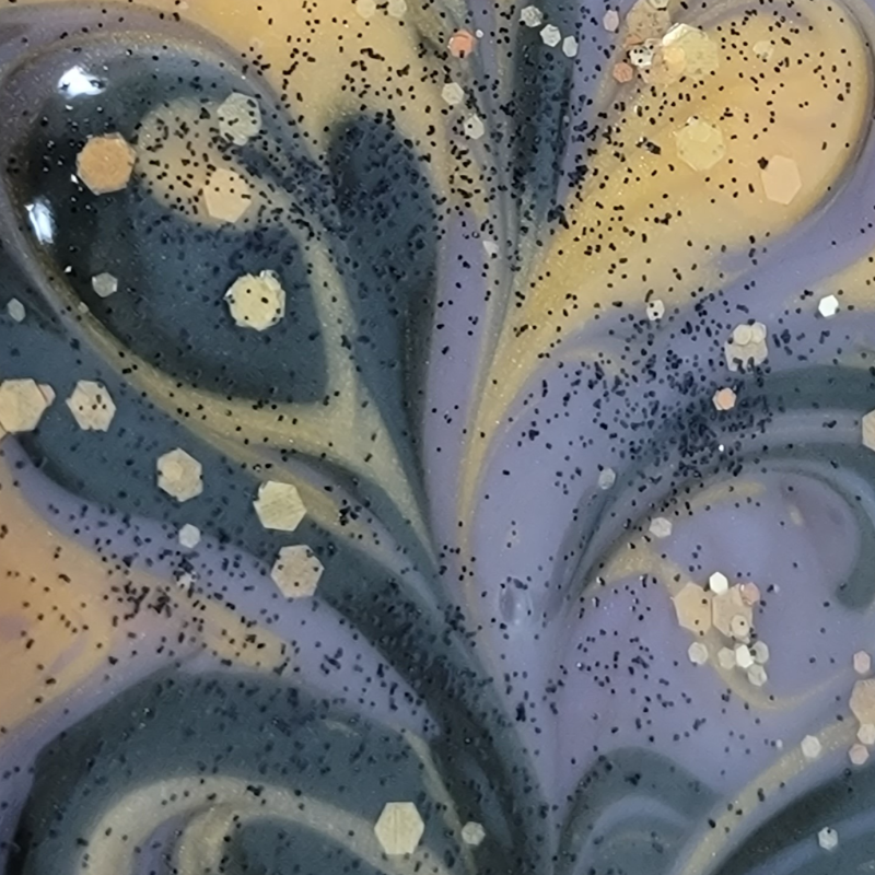 Close-up of the top of wet soap with gold, black and purple swirls, along with gold and black glitter