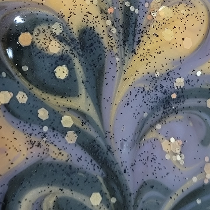 Close-up of the top of wet soap with gold, black and purple swirls, along with gold and black glitter