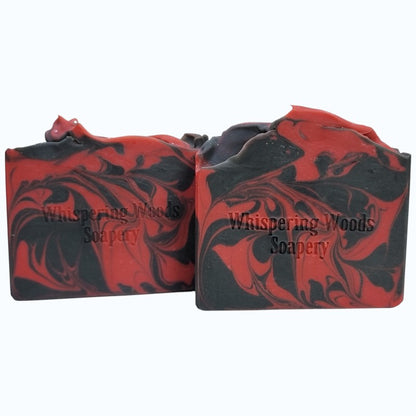 Two bars of red and black marbled soap with 'Whispering Woods Soapery' branding on a white background