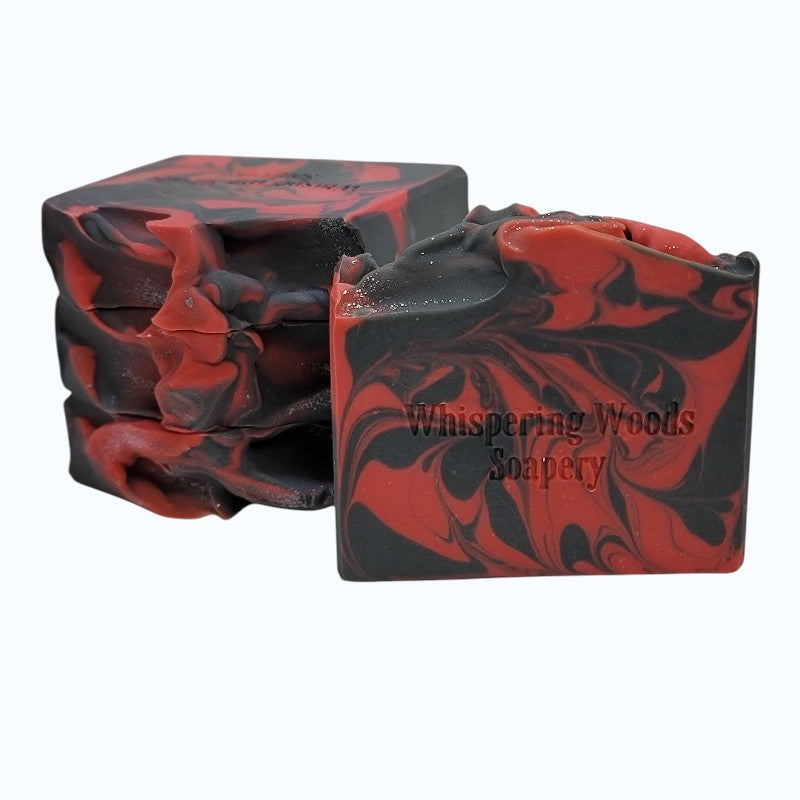 Four bars of red and black marbled soap with 'Whispering Woods Soapery' branding on a white background