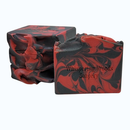 Four bars of red and black marbled soap with 'Whispering Woods Soapery' branding on a white background