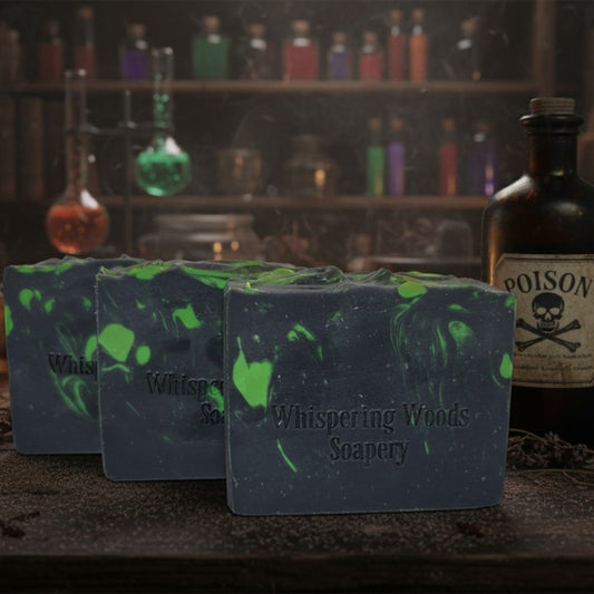 Three bars of soap with green and black marbled pattern in front of a shelf with bottles, labeled 'Whispering Woods Soapery'
