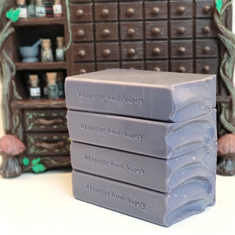 Four stacked purple bars of soap on a white surface in front of a miniature 3D printed apothecary cabinet.