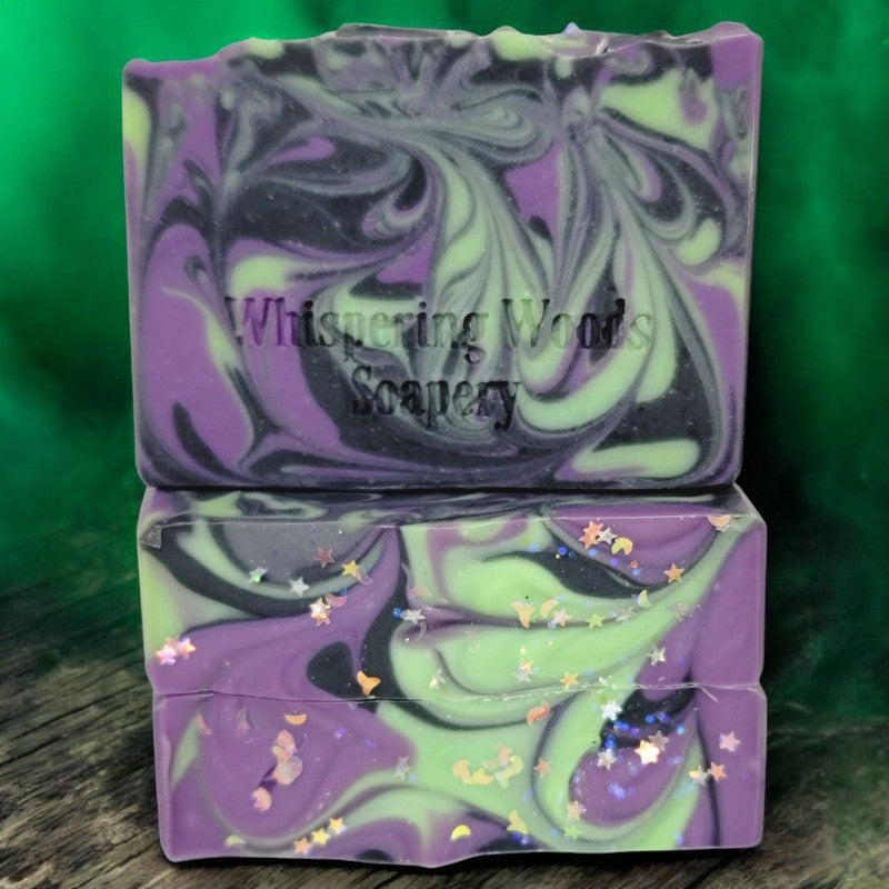 Three bars of soap with delightful purple, black and green swirls. The tops have glitter moons and stars. There is green magical fog in the background.