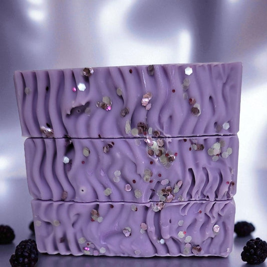 Purple soap with glittery texture and blackberries on a reflective surface