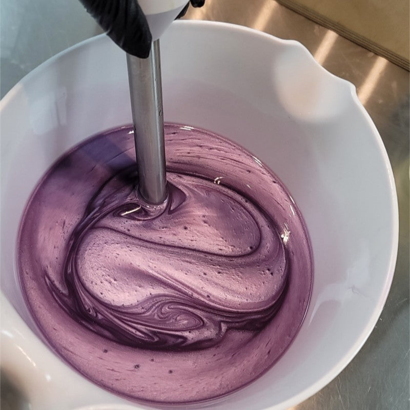 Shimmery purple oils being stirred by a stick blender