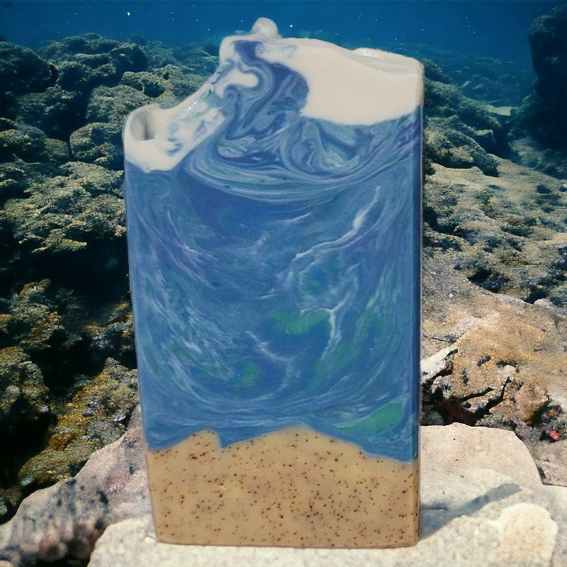 An ocean-themed bar of soap (watery top and bottom third sand) sits on a coral reef