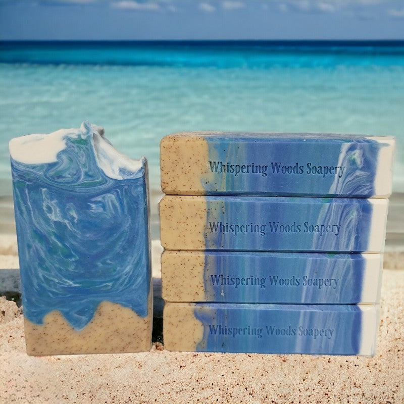 Five ocean-themed bars of soap on a beach with water in the background