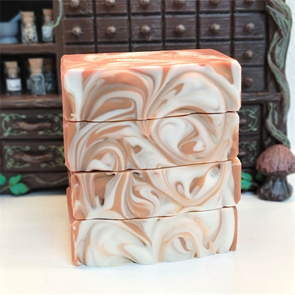 Four stacked rectangular bars of handmade soap with a marbled swirl pattern in caramel and white, set against a blurred background of a brown apothecary cabinet.