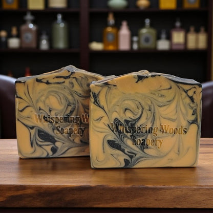 Two soap bars with a marbled design on a wooden surface, branded 'Whispering Woods Soapery'