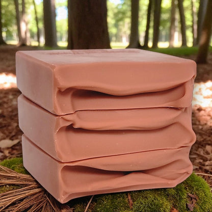 Stack of dusty pink soap bars on a green mossy surface with a forest background