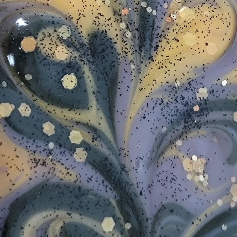 Extreme close-up of freshly poured gold, purple and black swirled soap with gold and black glitter on top