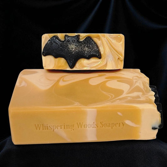 Two soap bars with a bat design on a black background, branded 'Whispering Woods Soapery'
