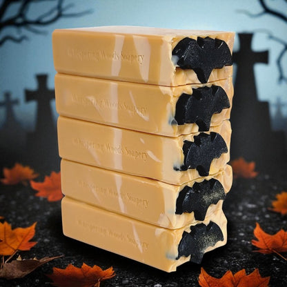 Stack of Halloween-themed soap bars with black bats on top, with a dark background with cross gravestones and leaves
