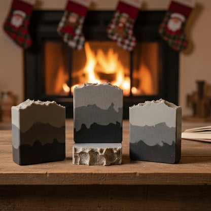 Four soap bars with gray layers on a wooden surface with a fireplace and stockings in the background