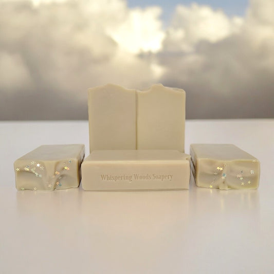 Five bars of yellowish-beige soaps with glitter stars on top on a white surface with clouds in the background