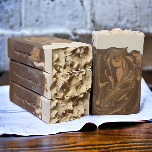 Four bars of copper and brown colored beer soap sitting on paper on a wood table