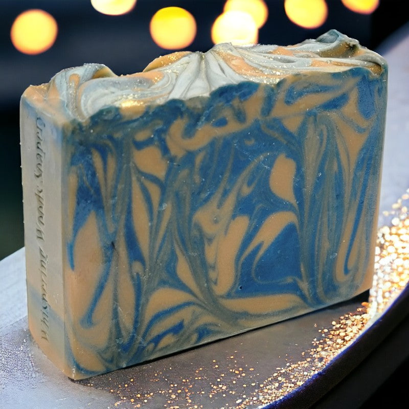 A bar of gold and blue soap sitting on a gold-flecked counter with blurry lights in the background