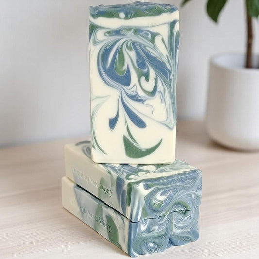 Three bars of white soap, with blue and green swirls, sit on a light wood counter