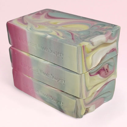 Three bars of light green, white, yellow, and pink swirled soap bars stacked on top of each other on a light pink background