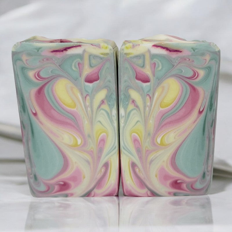 Two bars of light green, white, yellow, and pink swirled soap bars side by side on a white surface