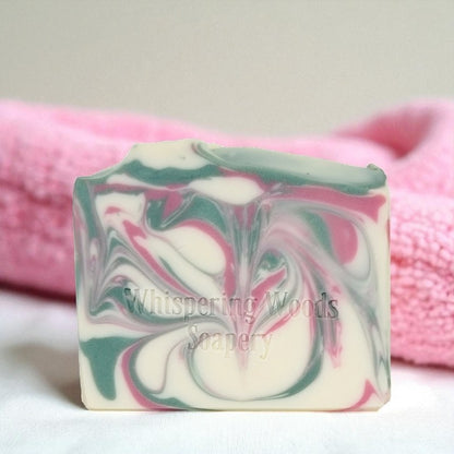 Swirled soap bar with 'Whispering Woods Soapery' branding on a pink towel background