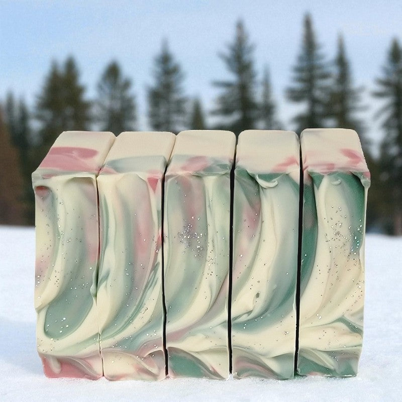 Five bars of soap with a green and pink swirled pattern on a snowy background with trees