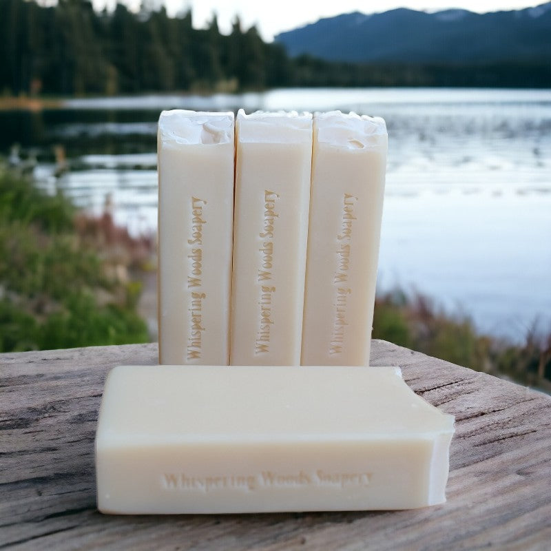 Four bars of cream-colored soap on a piece of wood by a lakeshore