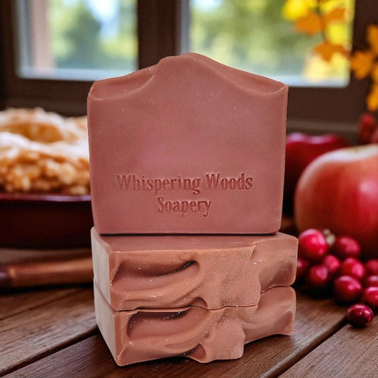 Three berry pink soap bars from Whispering Woods Soapery on a wooden surface with autumn decorations in the background