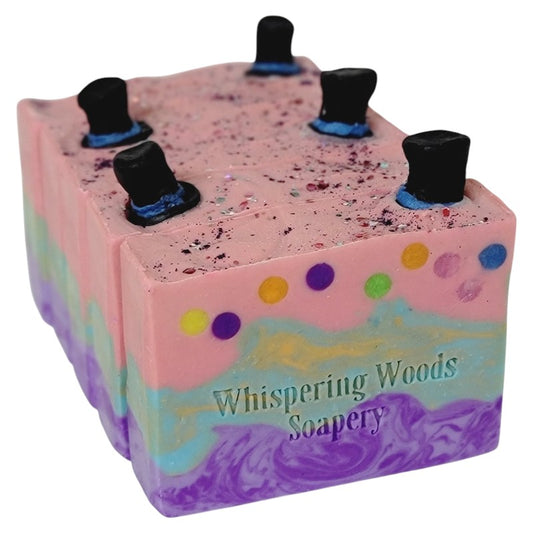 Four bars of pink, teal and purple soap, with glitter and small black top hats on top