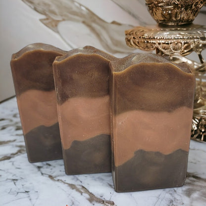 Three bars of soap on a marble countertop. The bottom layer is bronze brown, the middle layer is copper, and the top layer is a caramel-gold color.