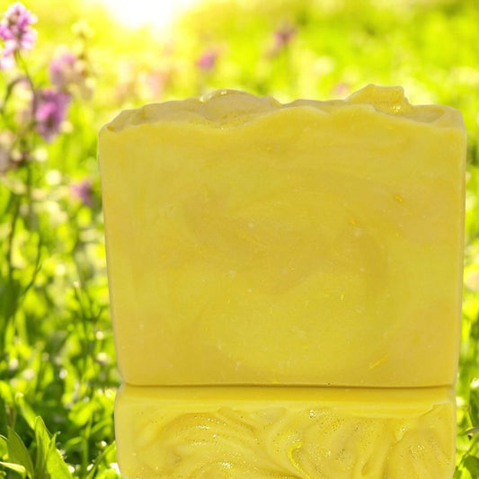 Two bars of swirled yellow soap sit in a sun-filled meadow with flowers